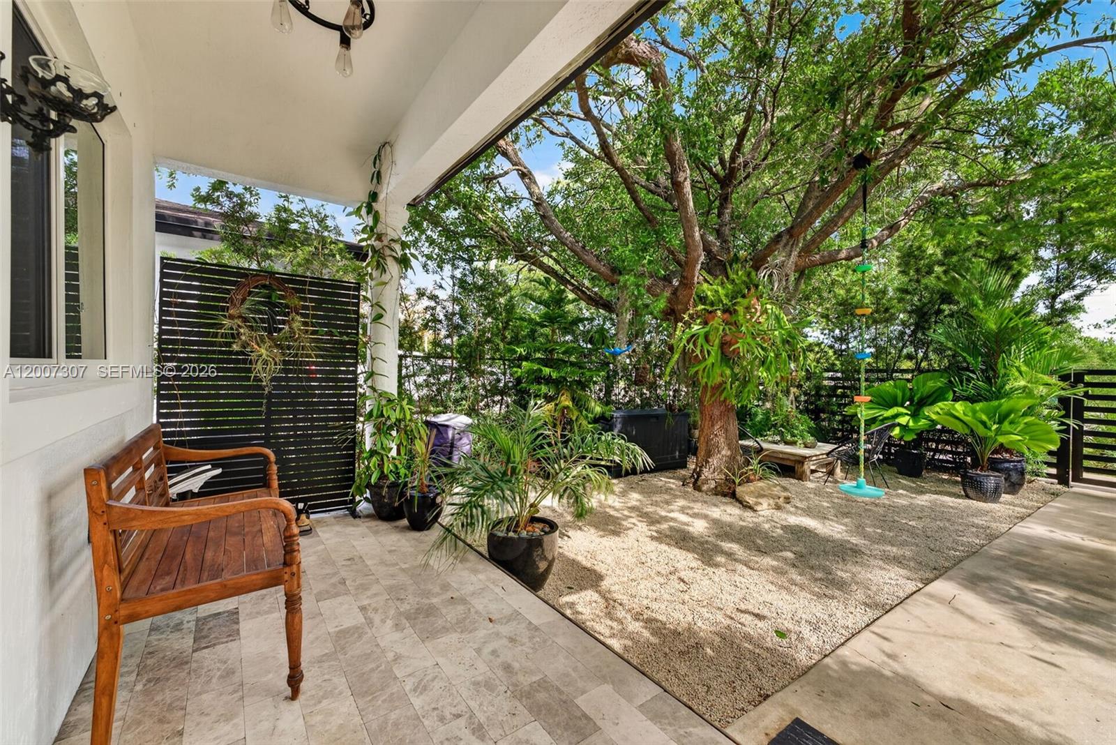 A covered patio features a wooden bench, stone flooring, and a gravel yard with trees — 12310 SW 216th St, Miami FL 33170, MIAMI, FL