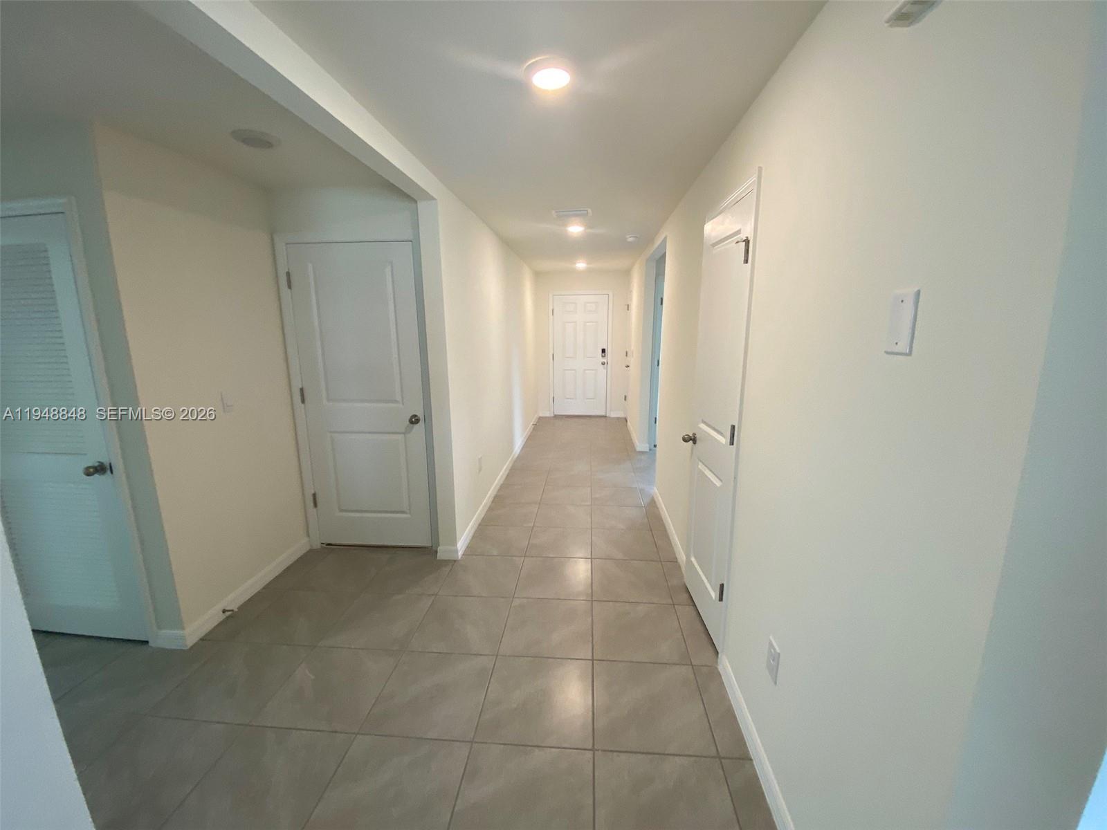 A hallway with light-colored walls and large square floor tiles leads to a white door — 8864 SW 49th CIRCLE, Ocala FL 34476, OCALA, FL