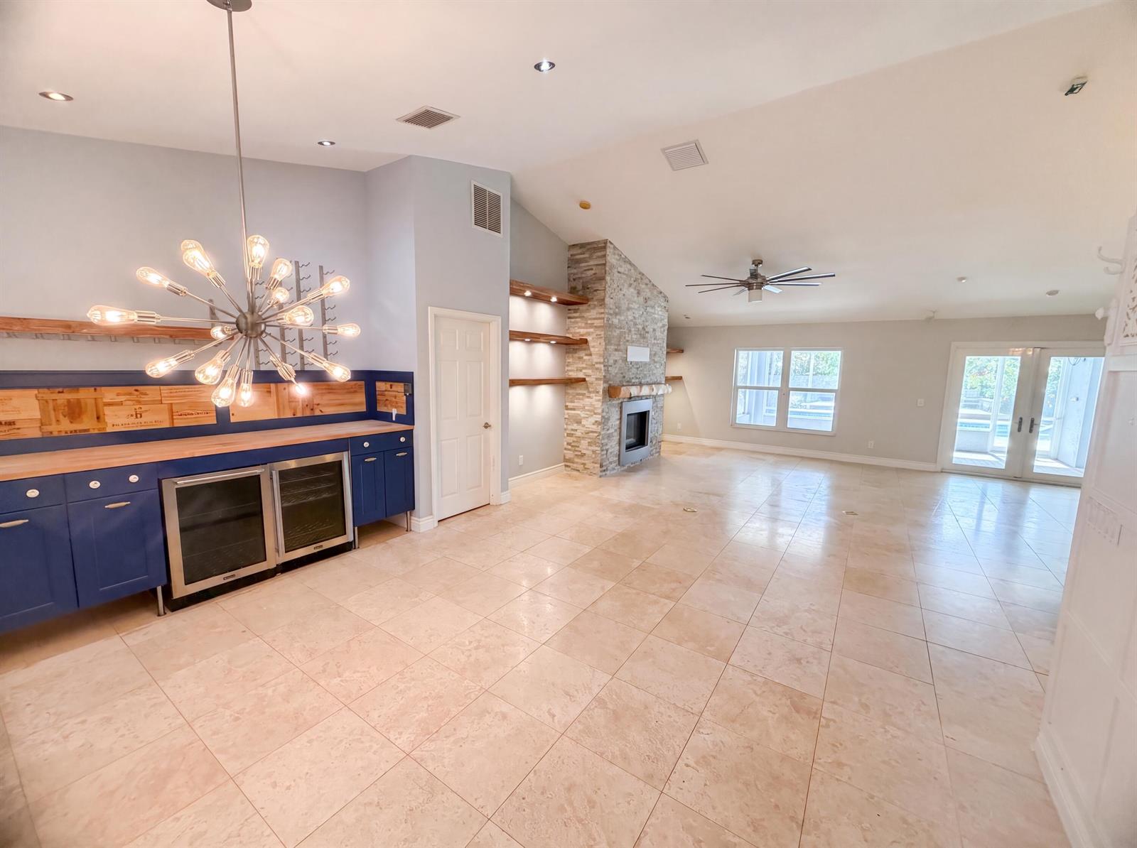 A spacious living area features a blue wet bar, stone fireplace, and light tile flooring — 2902 Serenity Circle S, Fort Pierce FL 34981, FORT PIERCE, FL