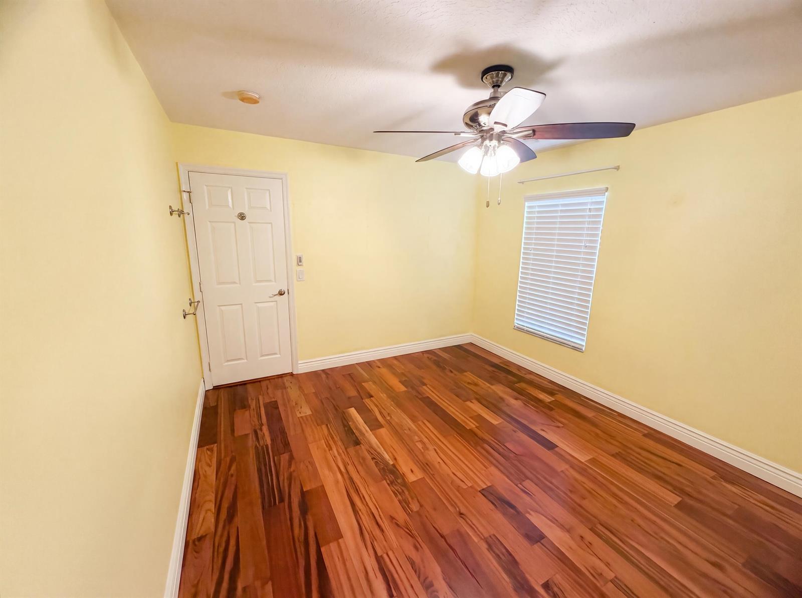 An empty room with yellow walls, wood flooring, a ceiling fan, and a white door — 2902 Serenity Circle S, Fort Pierce FL 34981, FORT PIERCE, FL
