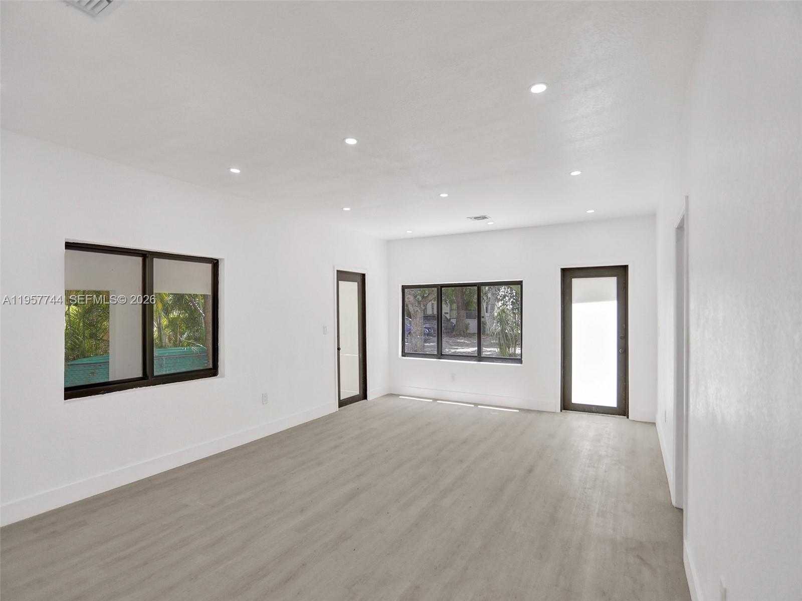 A bright, empty room features white walls, light wood-look flooring, recessed lighting, and dark-framed windows — 759 NE 127th St, North Miami FL 33161, NORTH MIAMI, FL