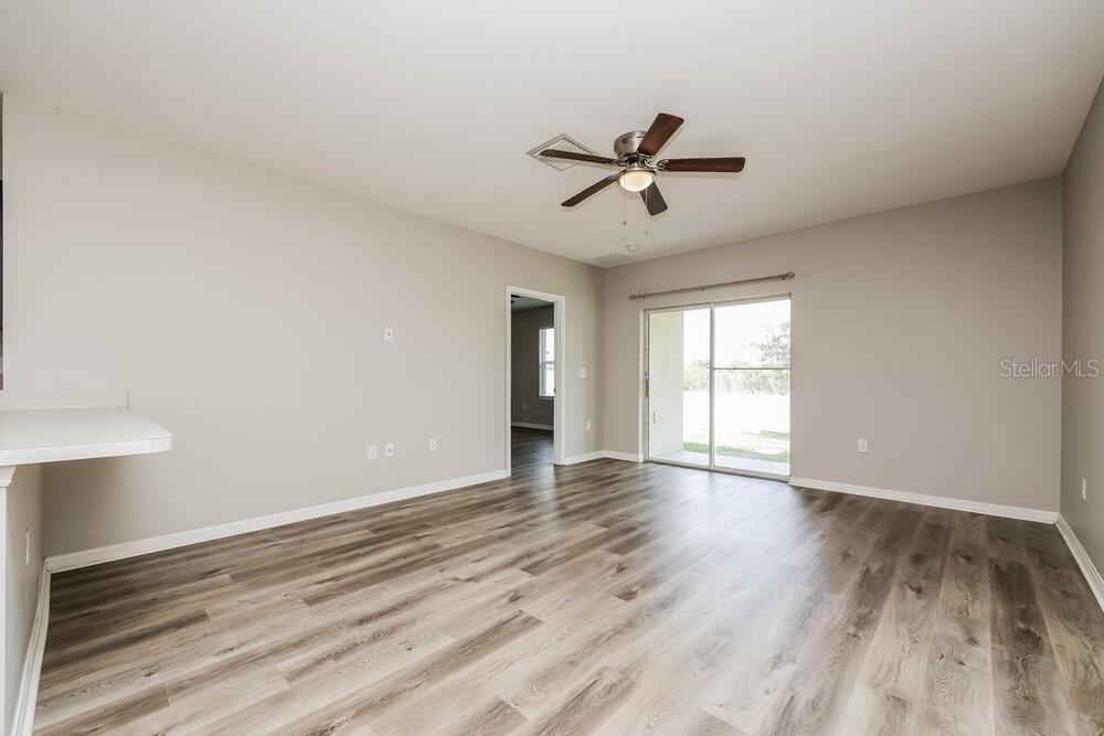 An empty living room features light gray walls, wood-look flooring, a ceiling fan, and sliding doors — 10540 WHISPERING HAMMOCK DRIVE, RIVERVIEW, FL