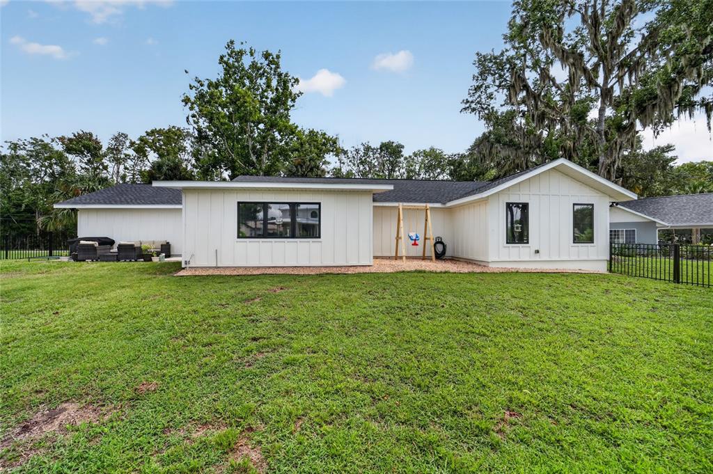 The exterior of a white, single-story house features vertical siding, black-framed windows, and a backyard — 232 SE KINGS BAY DR, CRYSTAL RIVER, FL