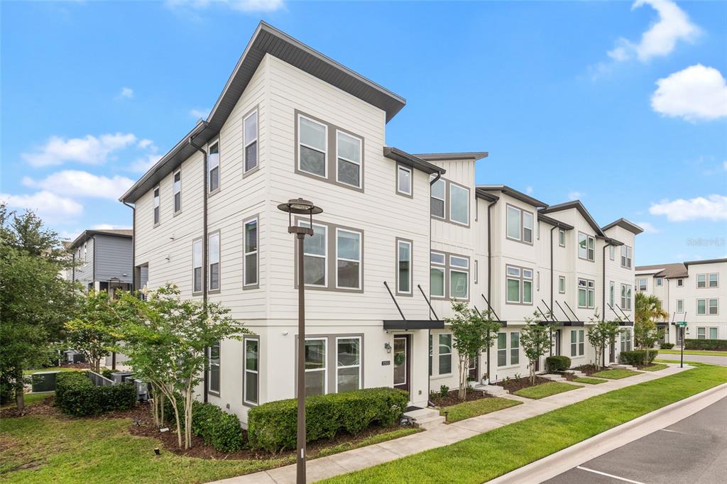 A multi-story townhouse with white siding and dark trim sits along a sidewalk — 12551 WILLSTATTER AVENUE, ORLANDO, FL