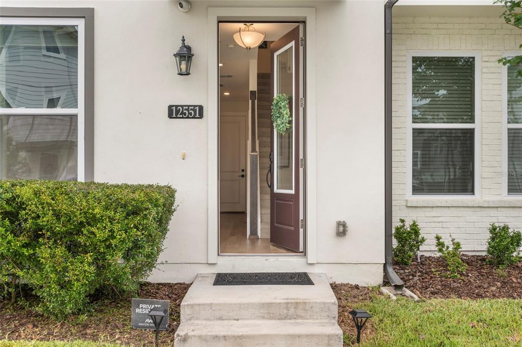 The exterior of a home features a white facade, a brown front door, and landscaping — 12551 WILLSTATTER AVENUE, ORLANDO, FL