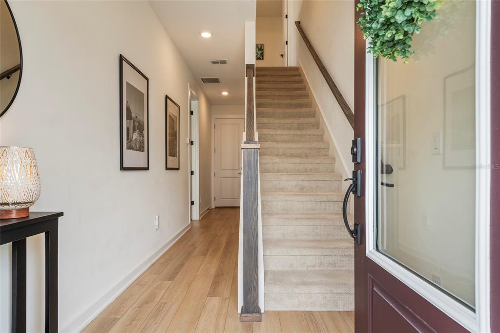An entryway features light wood flooring, a carpeted staircase with a dark railing, and framed art — 12551 WILLSTATTER AVENUE, ORLANDO, FL