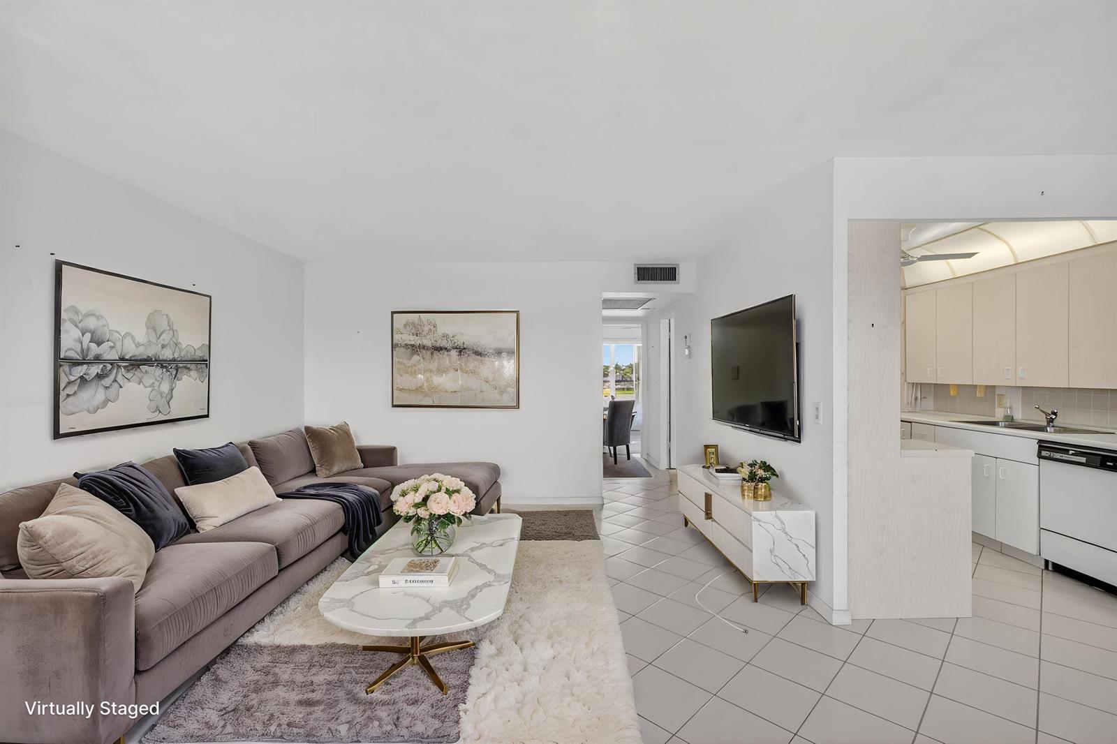 A living room with a gray sectional, marble coffee table, and an adjacent open kitchen — 4059 Guildford D, Boca Raton FL 33434, BOCA RATON, FL