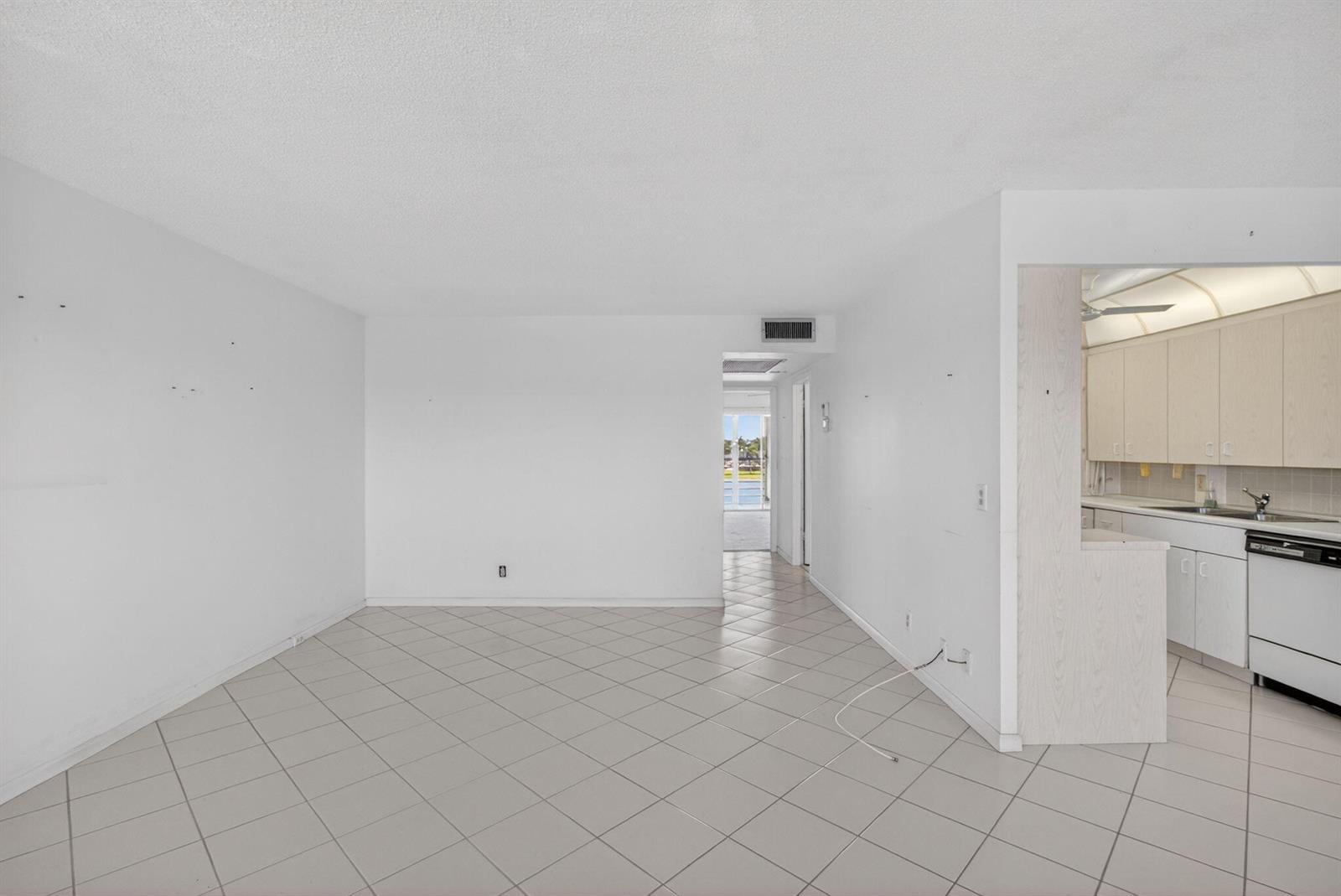 A white-walled living area with light-colored tile flooring leads to a kitchen and hallway — 4059 Guildford D, Boca Raton FL 33434, BOCA RATON, FL