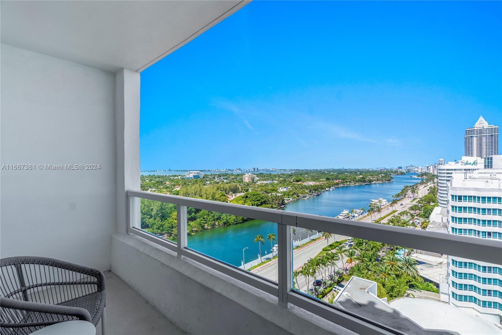 A balcony with a gray chair overlooks a waterway, palm trees, and city buildings — 4401 Collins Ave # 1709, Miami Beach FL 33140, MIAMI BEACH, FL