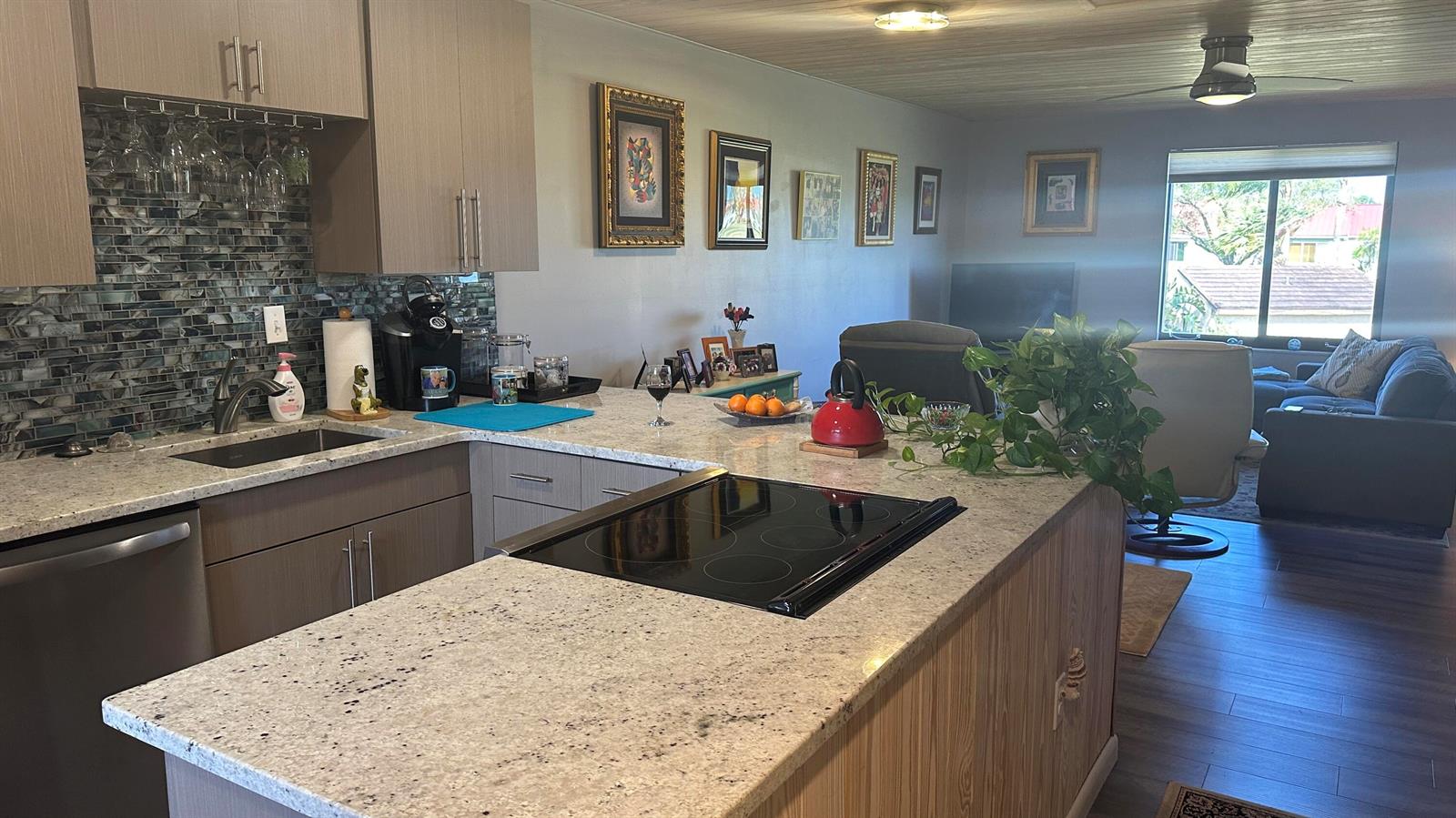 A kitchen with granite countertops, a glass cooktop, and a mosaic backsplash opens to a living area — 5355 SE Miles Grant Road # 209, Stuart FL 34997, STUART, FL
