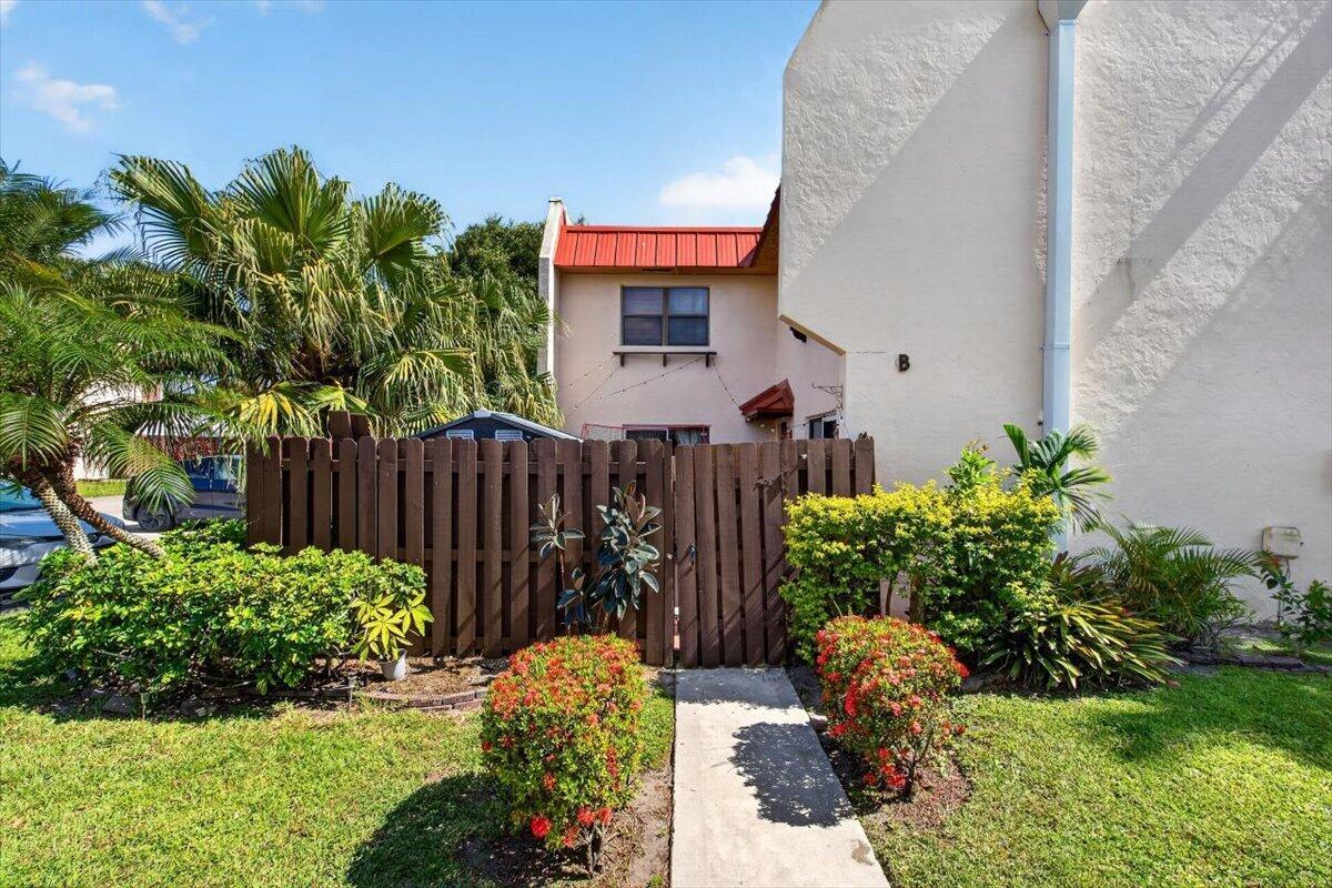 A tan two-story townhouse exterior with a red metal roof and a wooden privacy fence — 6351 Seven Springs Boulevard # B, FL 33463, FL