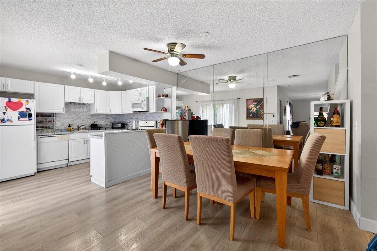 A dining area with a wooden table and chairs sits adjacent to a white kitchen — 6351 Seven Springs Boulevard # B, FL 33463, FL