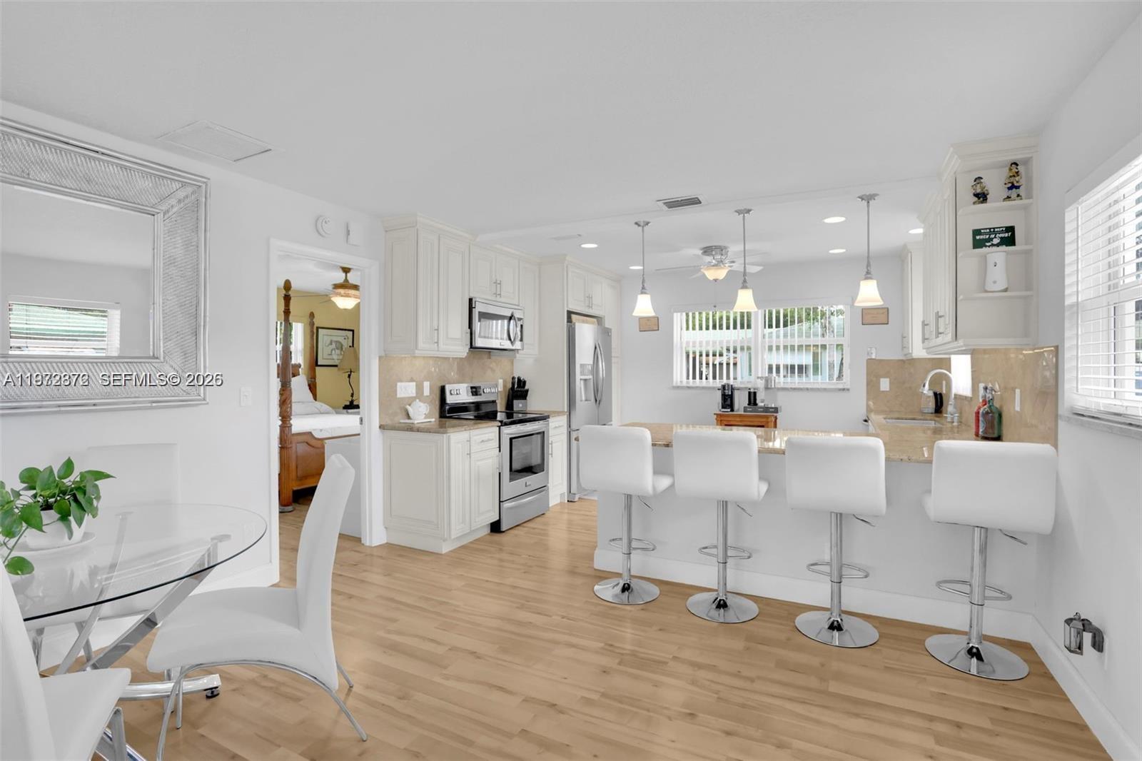 A bright kitchen features white cabinetry, stainless steel appliances, and a breakfast bar with stools — 841 Meadowlark Ln, Delray Beach FL 33445, DELRAY BEACH, FL