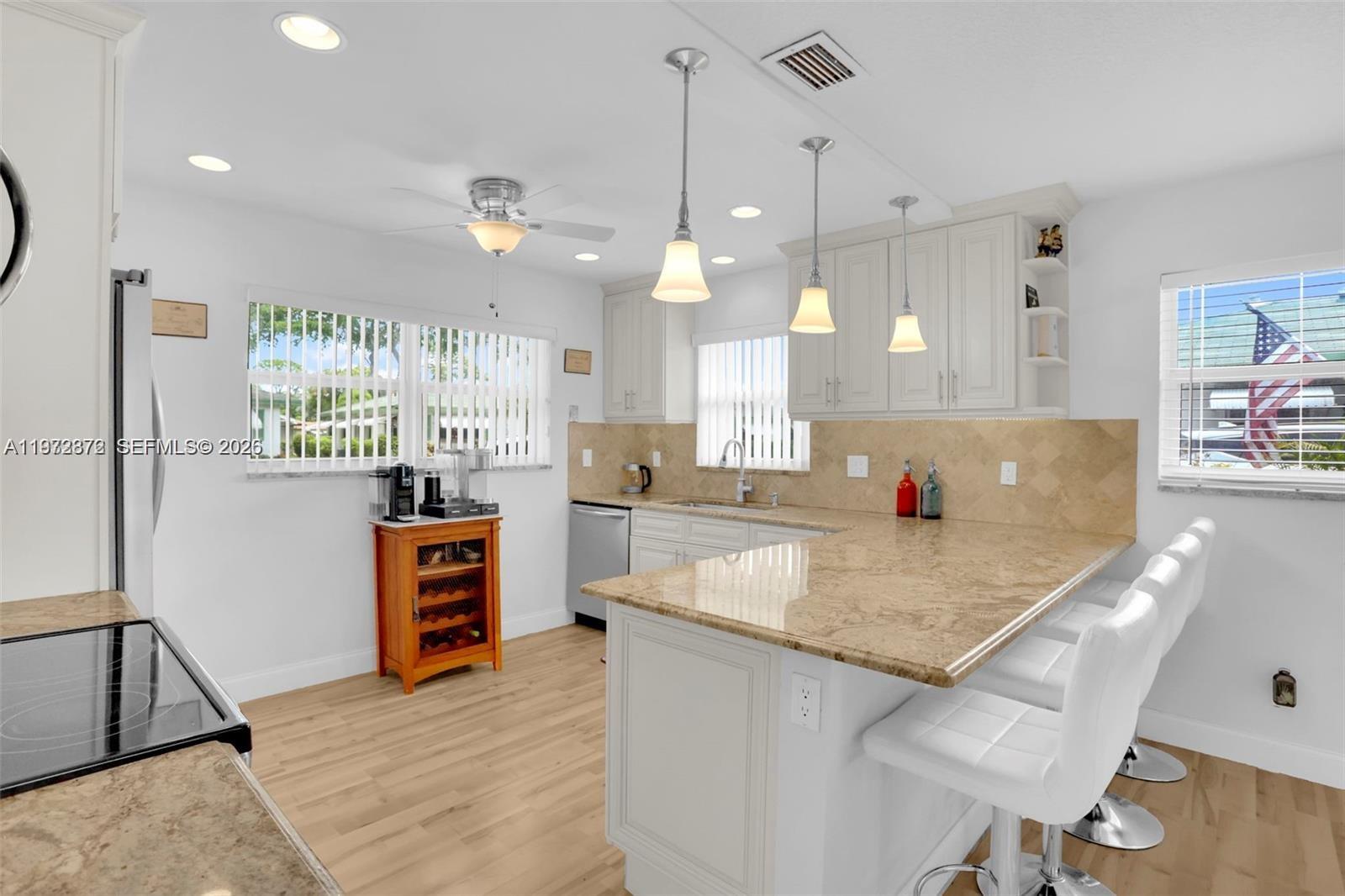 A kitchen features white cabinets, tan countertops, a breakfast bar with stools, and light flooring — 841 Meadowlark Ln, Delray Beach FL 33445, DELRAY BEACH, FL