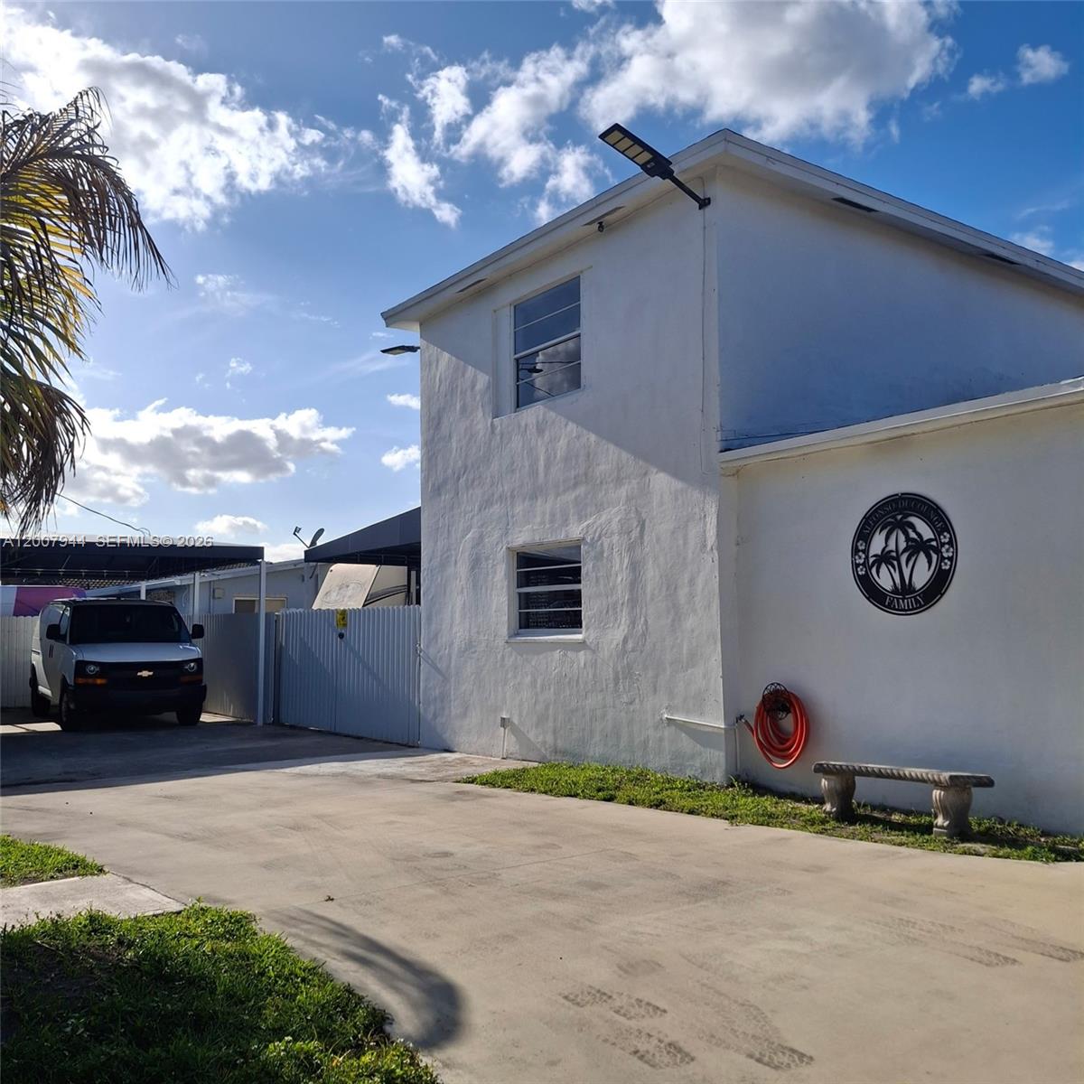 A two-story white building features a circular family sign, a hose, and a stone bench — 12215 SW 217th St, Miami FL 33170, MIAMI, FL