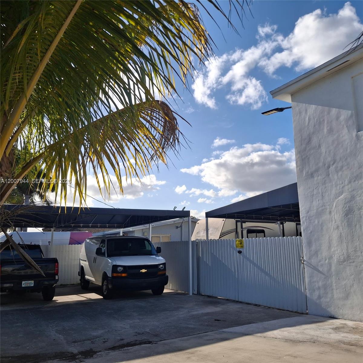 A white van and a black truck are parked under a carport beside a fence — 12215 SW 217th St, Miami FL 33170, MIAMI, FL