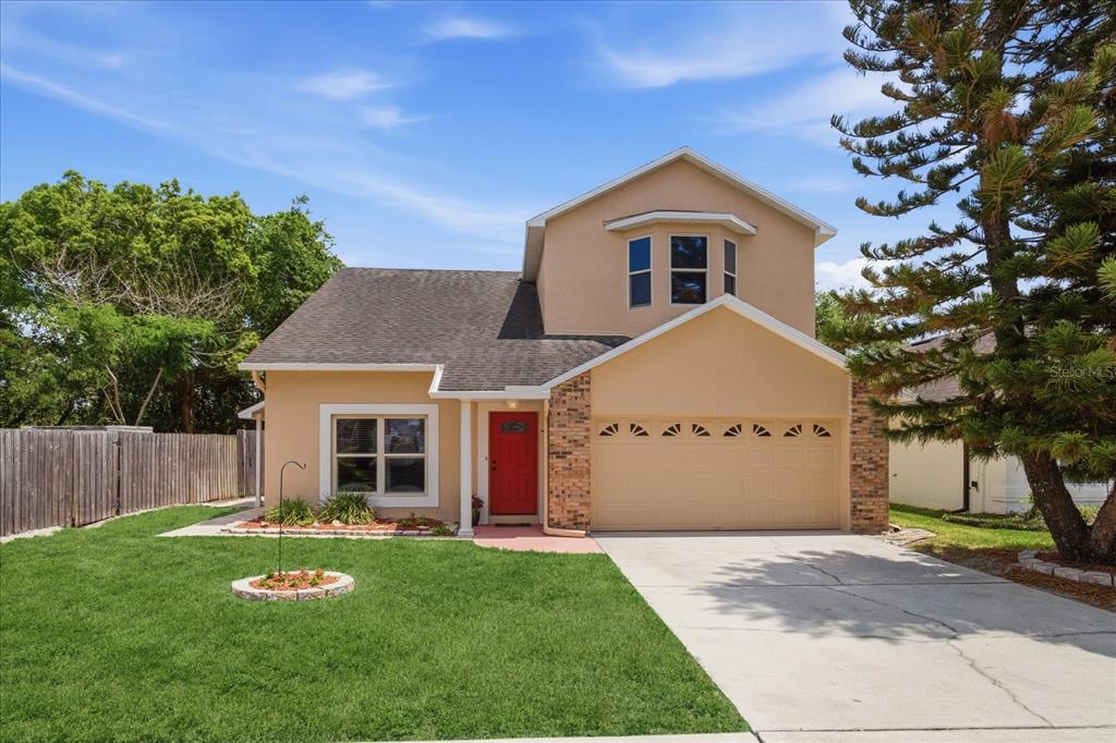 A two-story house with a tan exterior, a red front door, and a two-car garage — 1111 TWIN RIVERS BOULEVARD, OVIEDO, FL