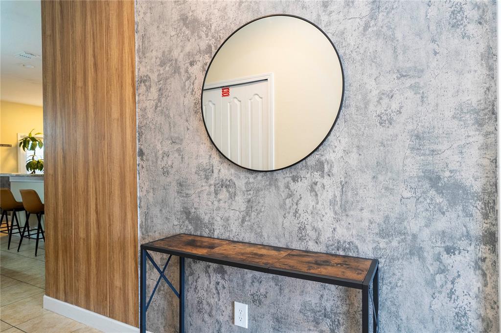 A console table sits against a concrete-textured wall beneath a round mirror — 8935 CANDY PALM ROAD, KISSIMMEE, FL