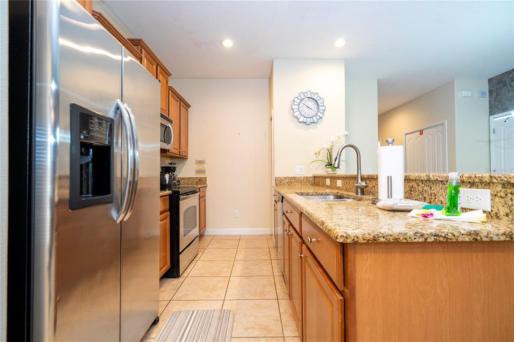 A kitchen features stainless steel appliances, wood cabinets, and granite countertops with a tile floor — 8935 CANDY PALM ROAD, KISSIMMEE, FL