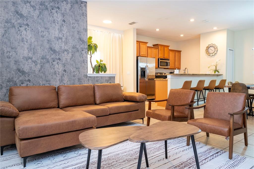 A living room with a brown sectional and two chairs sits before an open kitchen — 8935 CANDY PALM ROAD, KISSIMMEE, FL