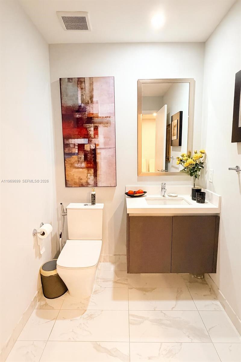 A modern half bathroom features a floating vanity, a toilet, and abstract wall art — 851 NE 1st Ave # 2212, Miami FL 33132, MIAMI, FL