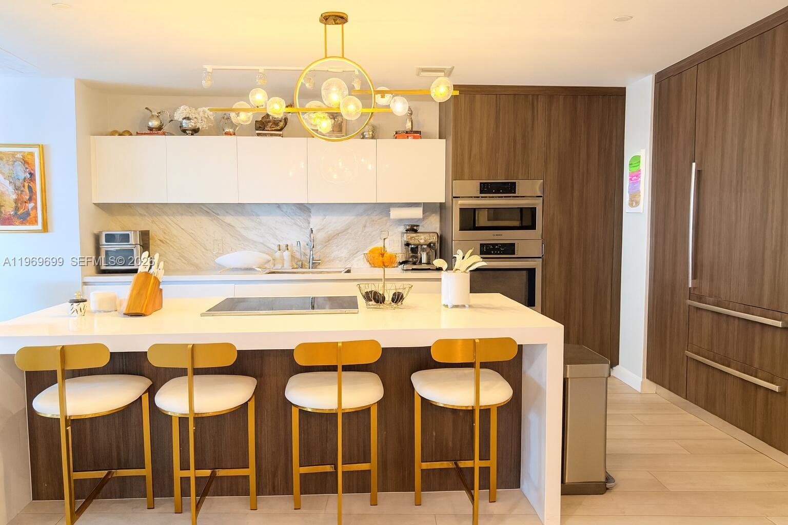 A modern kitchen features white cabinetry, a marble backsplash, a central island, and gold-accented stools — 851 NE 1st Ave # 2212, Miami FL 33132, MIAMI, FL