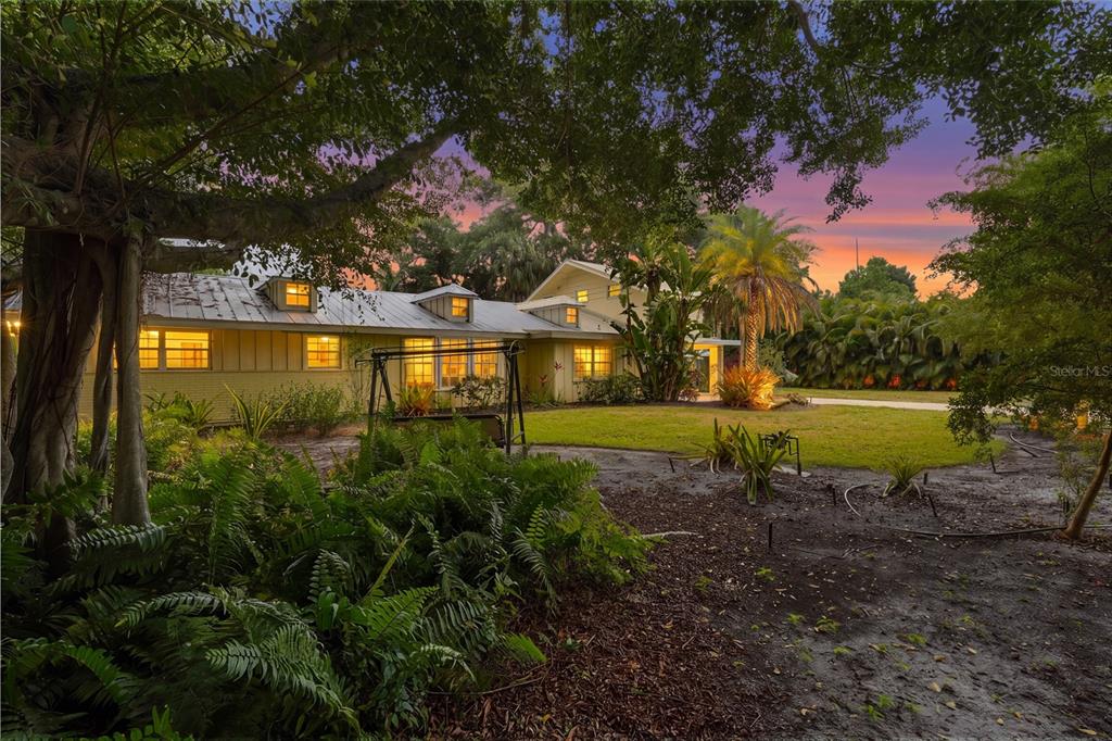 A yellow house with a metal roof sits behind lush landscaping at sunset — 2480 ALAMEDA AVENUE, SARASOTA, FL