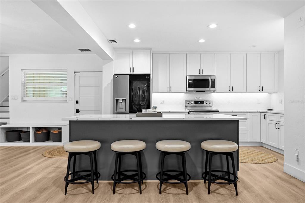 A modern kitchen features white cabinetry, a dark gray island with four stools, and light flooring — 2480 ALAMEDA AVENUE, SARASOTA, FL