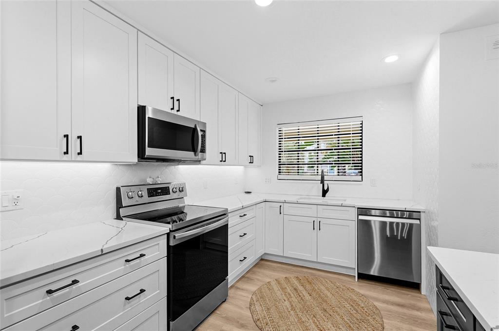A modern kitchen features white cabinets, stainless steel appliances, and white countertops with a backsplash — 2480 ALAMEDA AVENUE, SARASOTA, FL