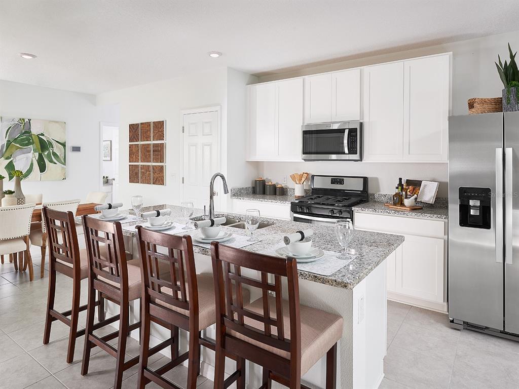A kitchen features white cabinets, granite countertops, stainless steel appliances, and a breakfast bar island — 9113 DALERA COVE, PALMETTO, FL