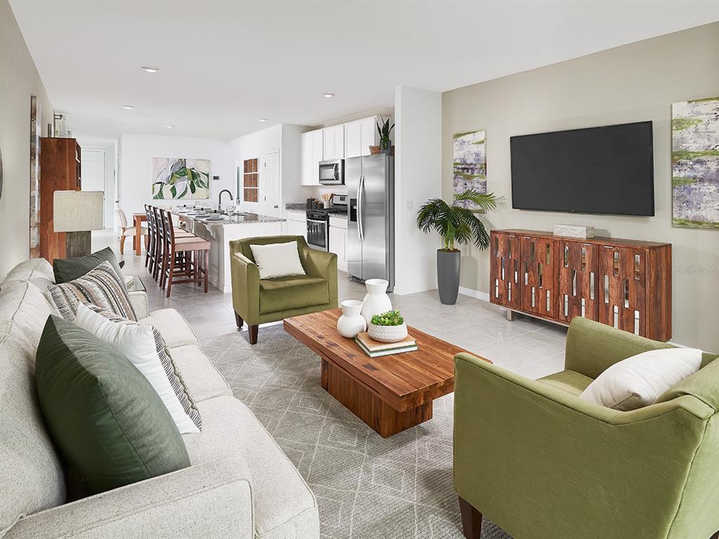 An open-concept living room and kitchen feature light tile floors, green armchairs, and wood furniture — 9113 DALERA COVE, PALMETTO, FL