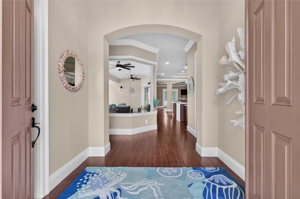 An entryway with a blue patterned rug, wood floors, and an arched doorway leading inside — 16 MONTILLA PLACE, PALM COAST, FL