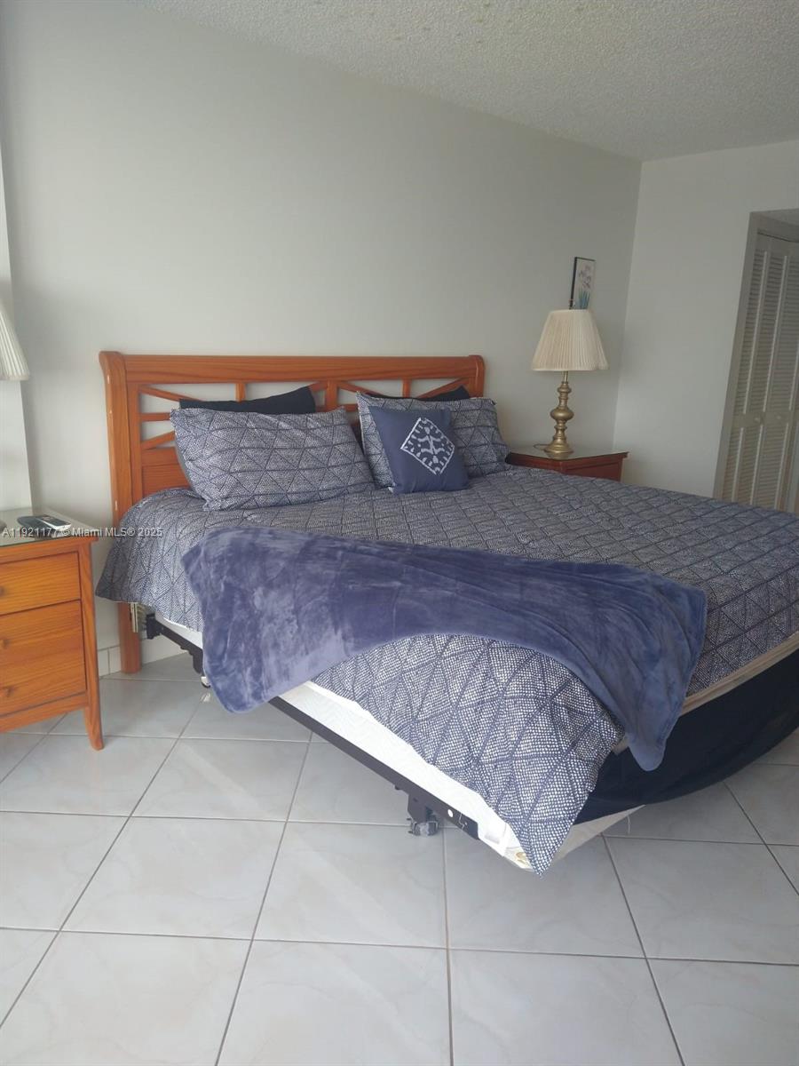 A bedroom features a wooden headboard, a patterned bedspread, and tile flooring — 9341 SE Collins Ave # 303, Surfside FL 33154, SURFSIDE, FL