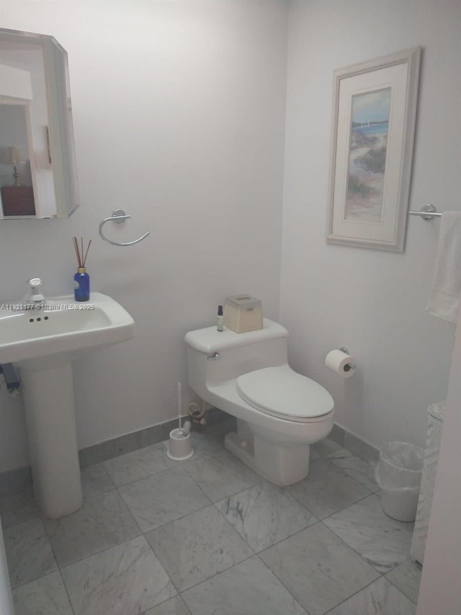A small bathroom features a pedestal sink, a white toilet, and light gray tiled flooring — 9341 SE Collins Ave # 303, Surfside FL 33154, SURFSIDE, FL