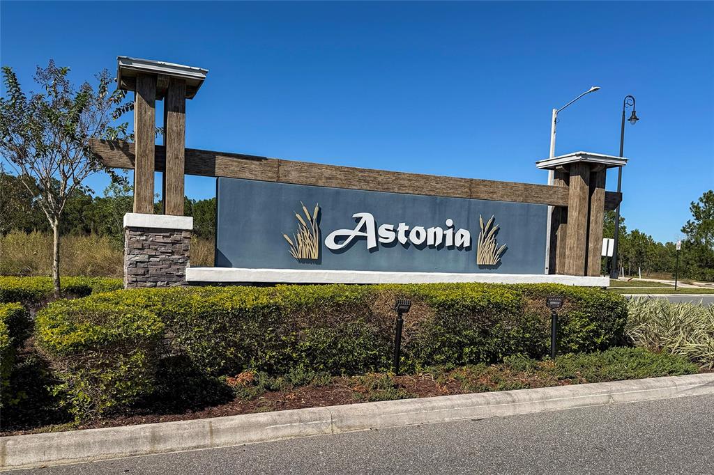 A stone and wood monument sign for the Astonia community stands behind a manicured hedge — 419 LILY LANE, DAVENPORT, FL