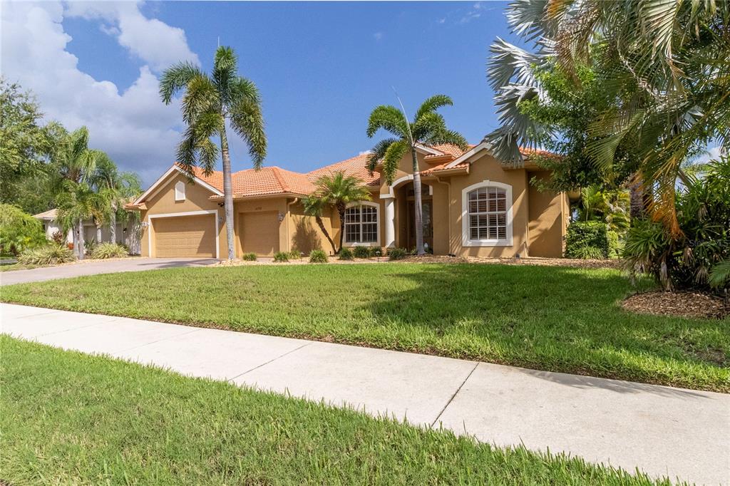 A single-story tan stucco house with a tile roof, three-car garage, and palm trees — 12709 PENGUIN DRIVE, BRADENTON, FL