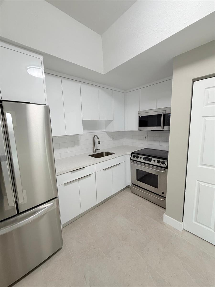 A modern kitchen features white flat-panel cabinets, stainless steel appliances, and light-colored countertops — 1390 W 37th Street # 101, Hialeah FL 33012, HIALEAH, FL