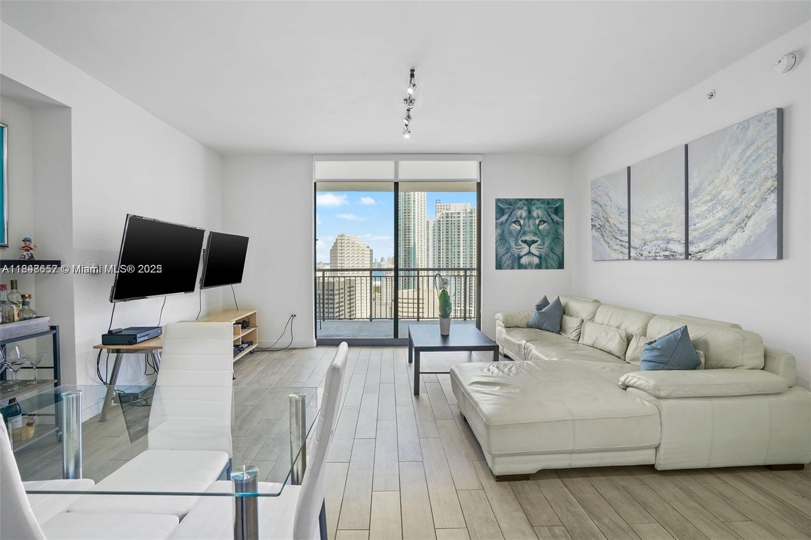 A modern living room features a white sectional sofa, glass dining table, and balcony view — 999 SW 1st Ave # 2717, Miami FL 33130, MIAMI, FL