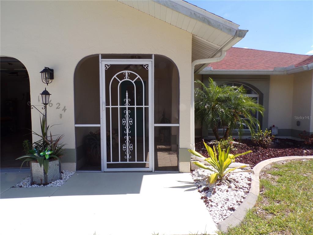 A front entryway features a white screen door, a concrete porch, and decorative landscaping — 15624 HENNIPEN CIRCLE, PORT CHARLOTTE, FL