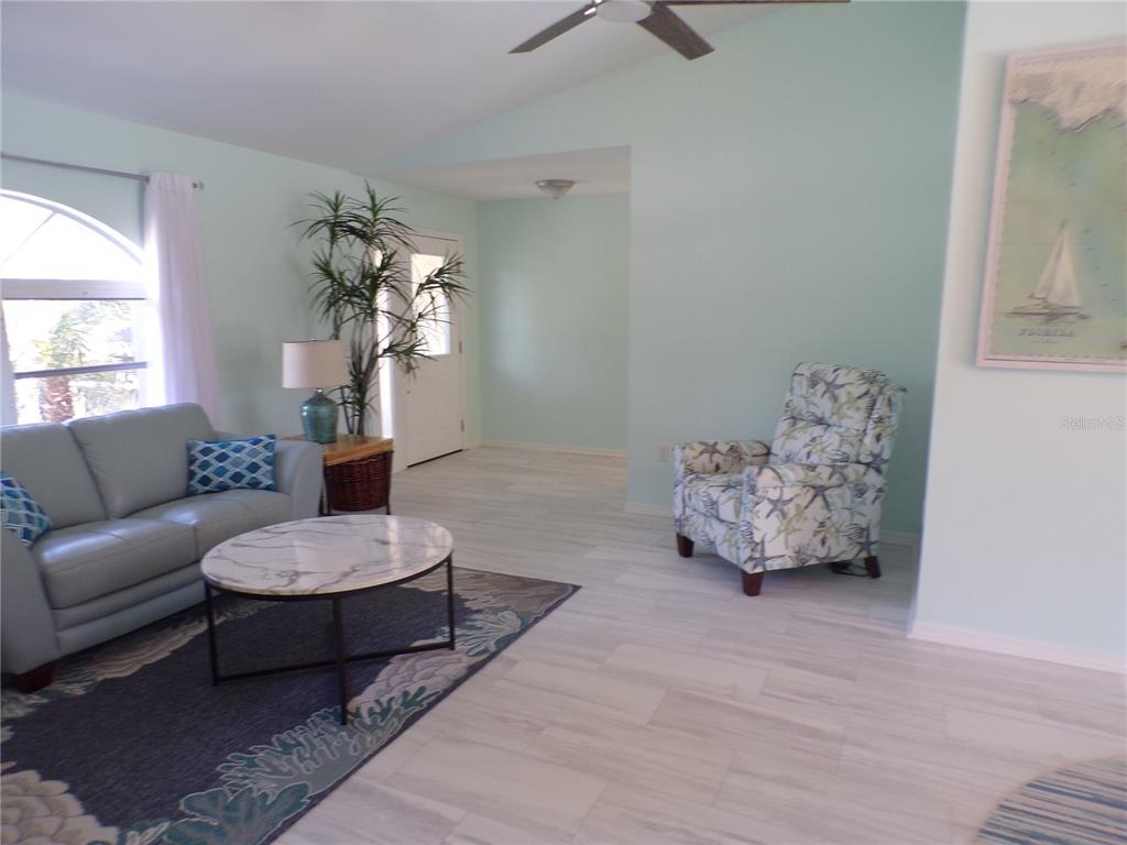 A living room features light blue walls, a gray sofa, a patterned armchair, and tile flooring — 15624 HENNIPEN CIRCLE, PORT CHARLOTTE, FL