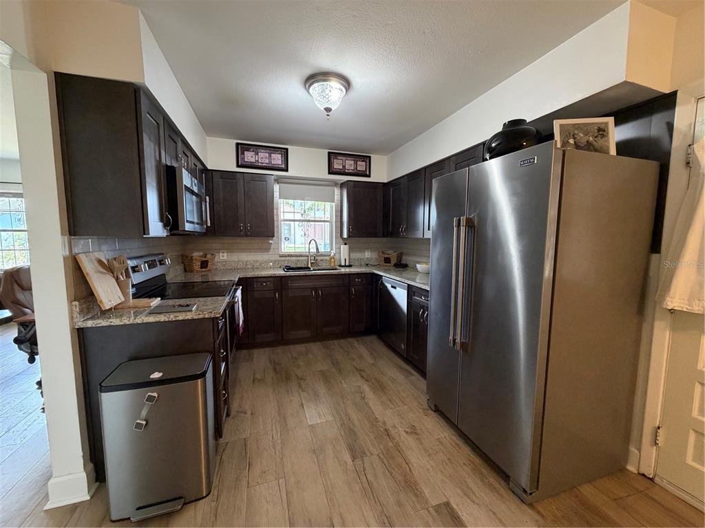 A kitchen features dark wood cabinets, granite countertops, stainless steel appliances, and wood-look tile flooring — 3230 W SAINT CONRAD STREET, TAMPA, FL