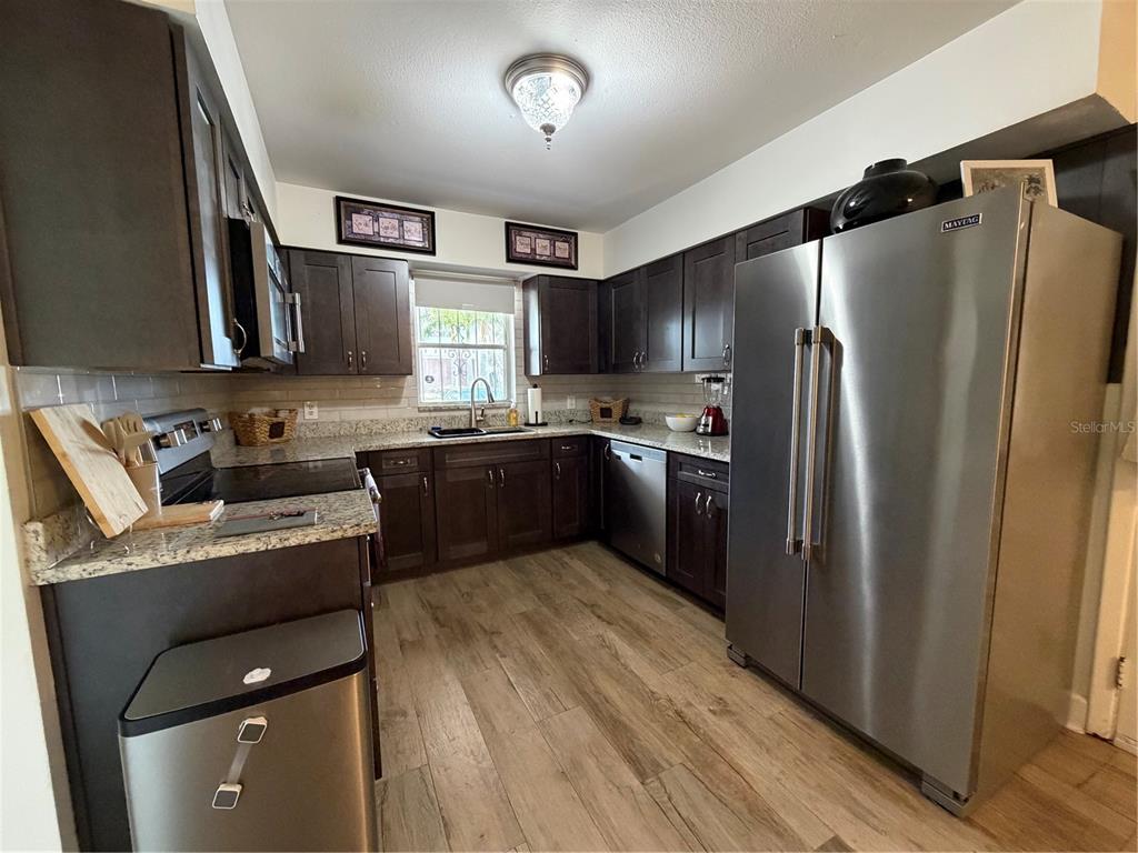 A kitchen features dark wood cabinets, stainless steel appliances, granite countertops, and wood-look flooring — 3230 W SAINT CONRAD STREET, TAMPA, FL
