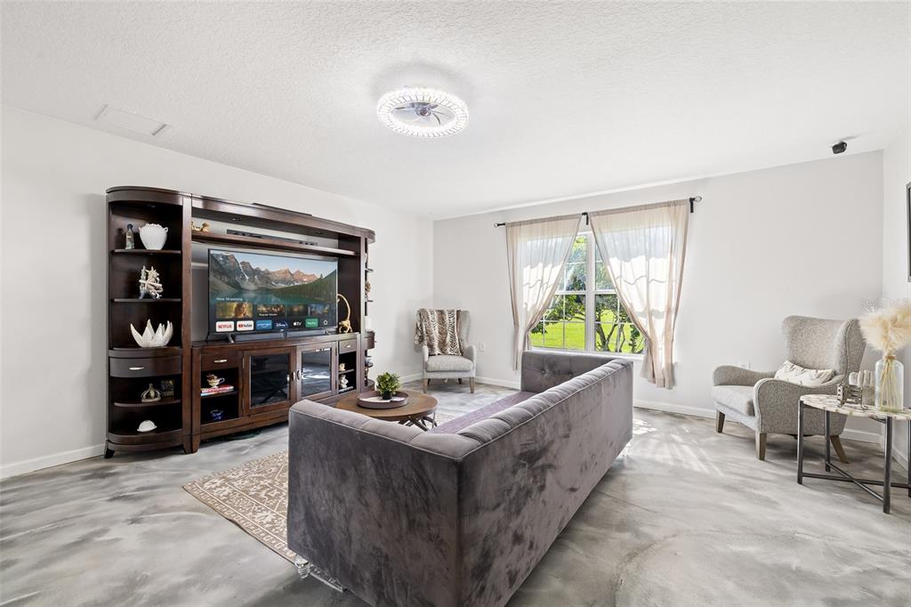 A living room features a dark wood entertainment center, grey sofa, and polished concrete floors — 4245 HENRY J AVENUE, ST CLOUD, FL