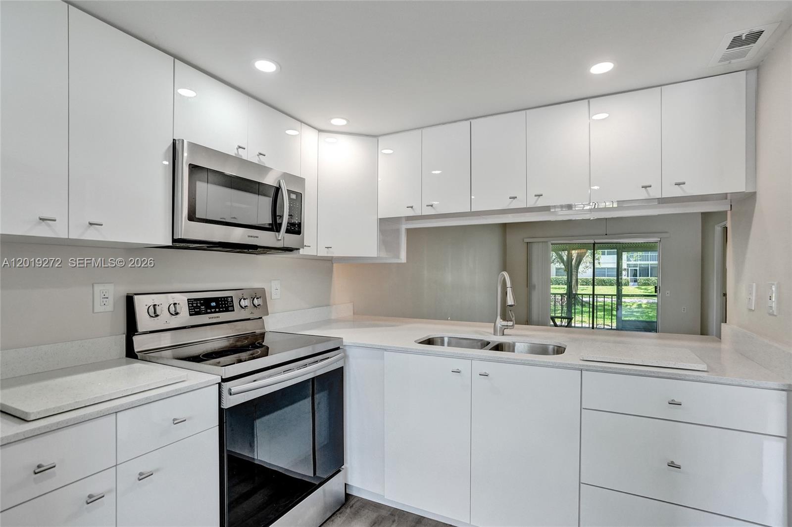 A modern kitchen features white cabinets, stainless steel appliances, and a pass-through window — 1108 Bahama Bnd # B1, Coconut Creek FL 33066, COCONUT CREEK, FL