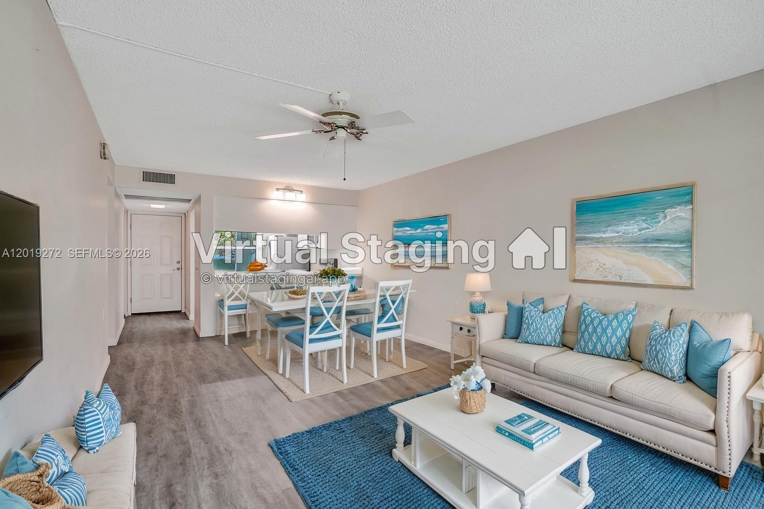 This living and dining room features light-colored furniture, blue accents, and wood-look flooring — 1108 Bahama Bnd # B1, Coconut Creek FL 33066, COCONUT CREEK, FL