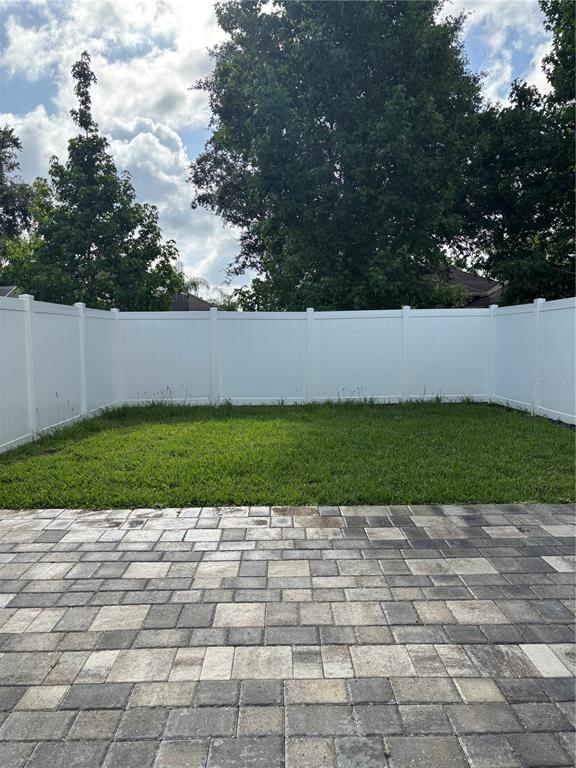 A paved patio overlooks a small grassy backyard enclosed by a white vinyl privacy fence — 1001 LA MIRADA COURT, KISSIMMEE, FL