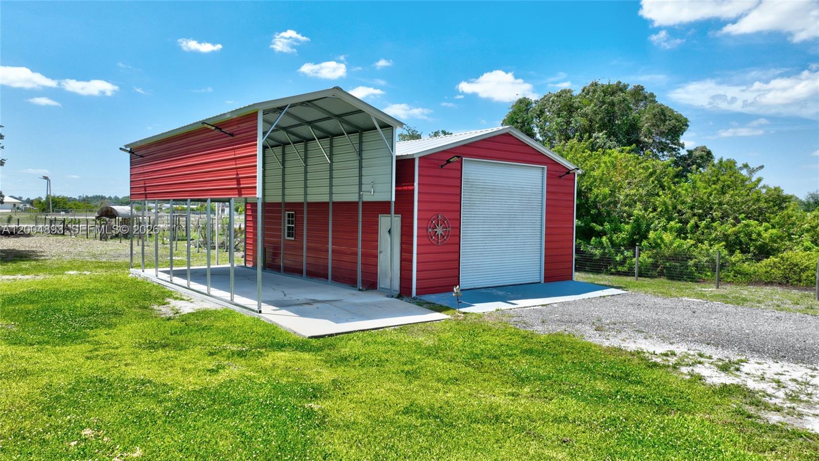 A red metal garage with an attached open-sided carport sits on a grassy lot — 7655 17th Place, La Belle FL 33935, LA BELLE, FL
