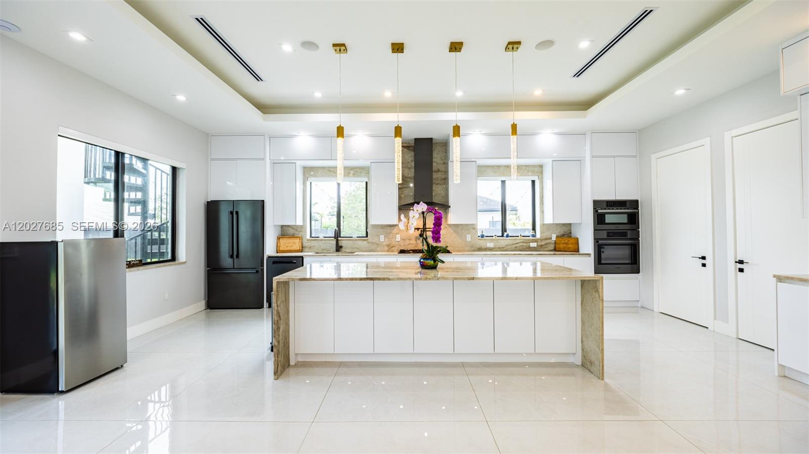 A modern kitchen features white cabinetry, a stone-topped island, and stainless steel appliances — 11450 SW 59th Ter, Miami FL 33173, MIAMI, FL