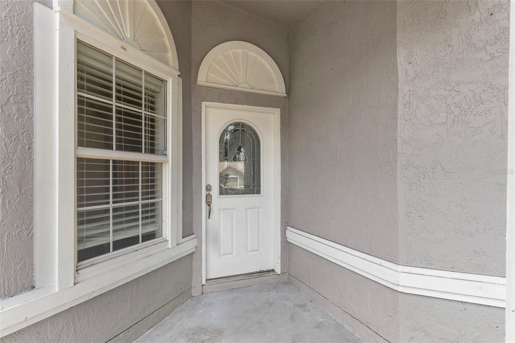 A white front door with a glass insert sits beside a window on a porch — 1969 SHEELER OAKS DRIVE, APOPKA, FL