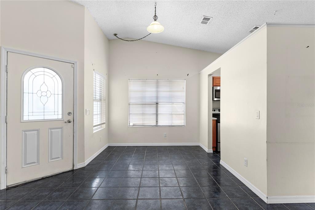 A dining area features dark tile flooring, a vaulted ceiling, and a white front door — 1969 SHEELER OAKS DRIVE, APOPKA, FL
